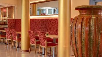 A restaurant with booths and red upholstered chairs, a large vase, and a mirror on the wall.