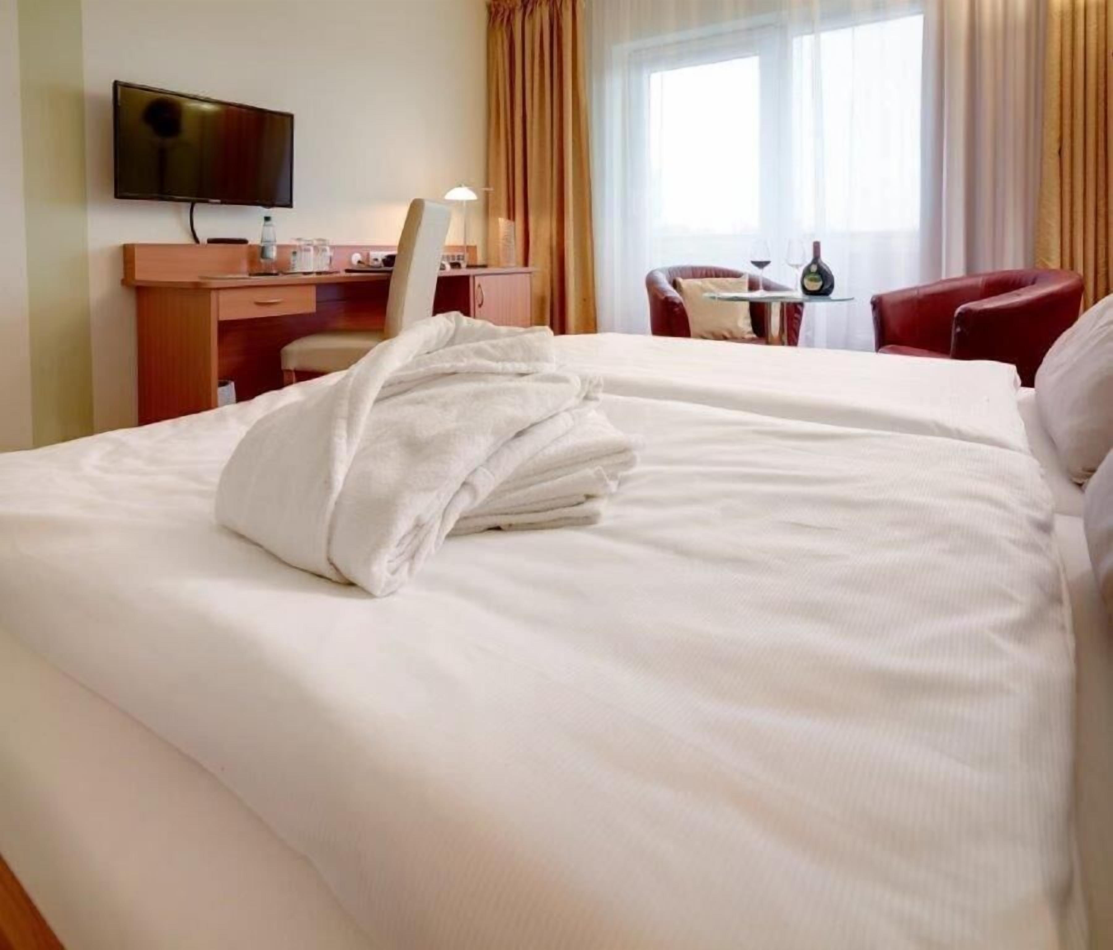 A hotel room with a bed, a desk with a chair, a television, and a window with curtains.