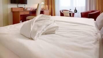 A hotel room with a bed, a desk with a chair, a television, and a window with curtains.