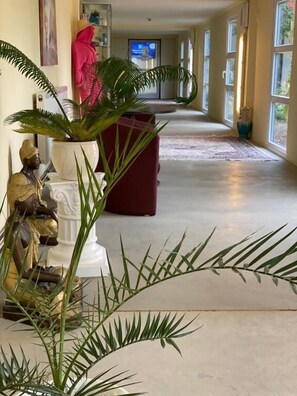 A hallway with a potted plant, a statue, and a red sofa. - Kurhotel Pyramide (Bad Windsheim)
