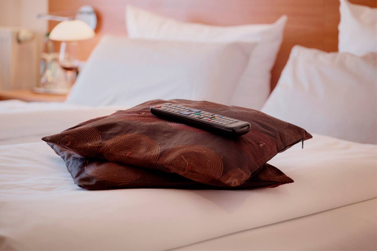 A neatly made bed with a remote control on a brown pillow.