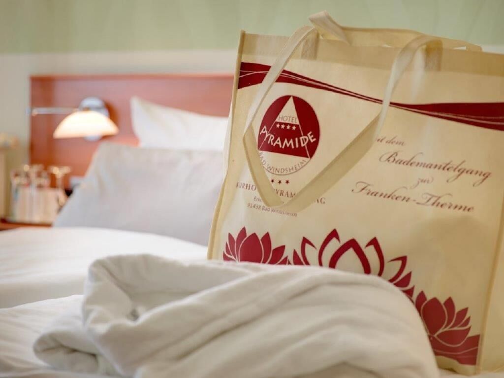 A hotel room with a bed, pillows, a lamp, and a bag with the hotel's logo.