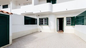 Ein mehrgeschossiges Wohngebäude mit weißen Wänden und grünen Fensterläden, mit einem gefliesten Innenhof und Balkonen.
