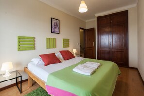 A bedroom with a bed, green wall art, a wooden wardrobe, and a framed picture on the wall.