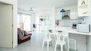 A modern kitchen with white cabinets, a dining area with white chairs, and a red sofa in the living room. - 126-APARTMENT WITH VIEWS OF THE PORT OF ROSES (Roses)