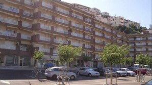 A multi-story residential building with balconies, parked cars, and small trees in the parking lot. - 126-APARTMENT WITH VIEWS OF THE PORT OF ROSES (Roses)