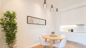 A modern kitchen with white cabinets, a round dining table with white chairs, and a potted plant.