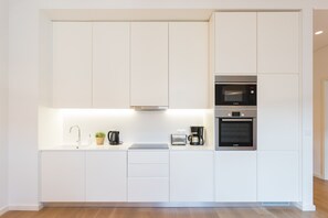 A modern kitchen with white cabinetry, a built-in microwave, an oven, a coffee maker, and a toaster.