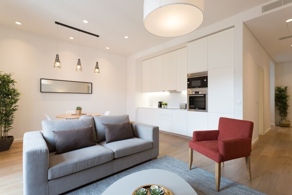 A modern living room with a grey sofa, a red armchair, a round coffee table, and a kitchen in the background.