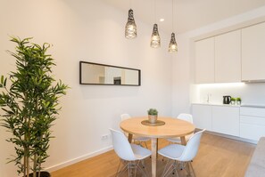 A modern kitchen with white cabinets, a round wooden table with white chairs, and hanging pendant lights.