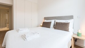 Un lit bien fait, avec des oreillers blancs et bruns, une table de chevet avec une lampe, et une pile de serviettes blanches posée sur le lit.