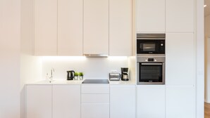 Une cuisine moderne avec des meubles blancs, une hotte en acier inoxydable, un four à micro-ondes de marque Bosch et un four traditionnel.