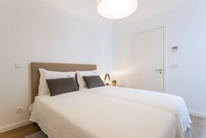 A double bed with white and gray bedding, a bedside lamp, and a small potted plant.
