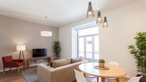 Un salon moderne avec un canapé, un téléviseur, une table à manger avec des chaises et des lampes suspendues.