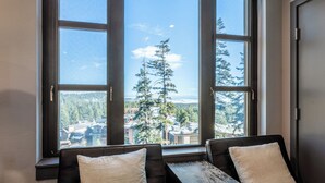 A room with a large window offering a view of a forest and distant buildings. There are two black leather chairs with cushions.