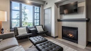 A modern living room with a fireplace, large windows, and a flat-screen TV.