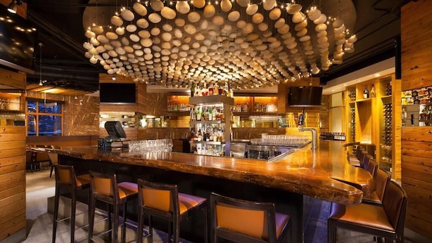 A bar area with a wooden bar counter, stools, and a unique ceiling light fixture.