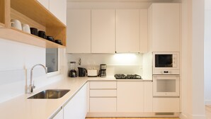 Una cucina moderna con mobili bianchi, un lavello in acciaio inossidabile, una macchina da caffè, un bollitore e un forno a microonde.