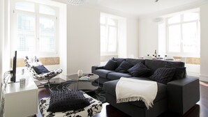 Uma sala de estar moderna com um sofá preto, uma poltrona estampada e uma mesa de centro.