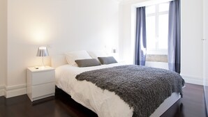 Quarto com cama, mesa de cabeceira e abajur.