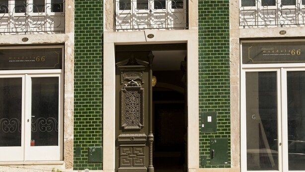 Fachada de edifício com padrão de tijolos verdes, entrada decorativa e duas portas com a inscrição 'mandala 66'.