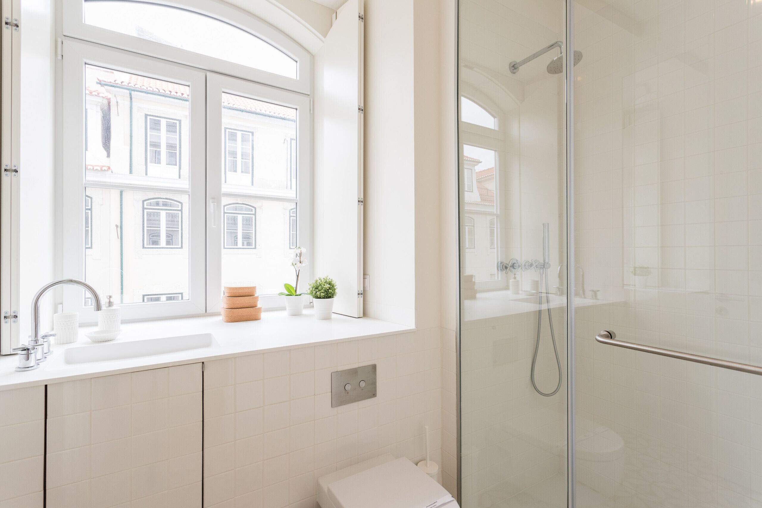A modern bathroom with a glass shower, a sink with a mirror, and a window with a view of buildings.