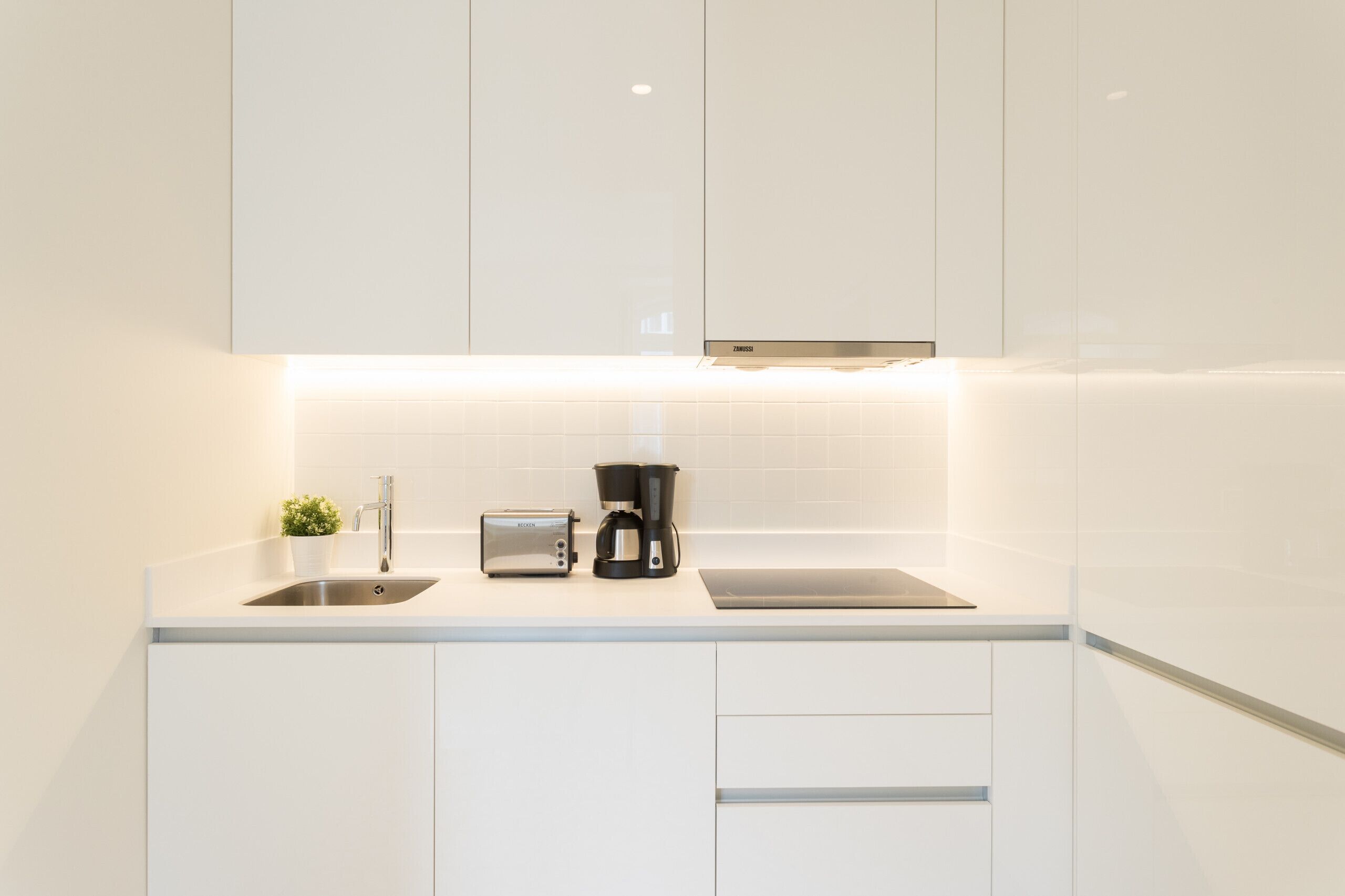 A modern kitchen with white cabinetry, a stainless steel sink, a toaster, and a coffee maker.