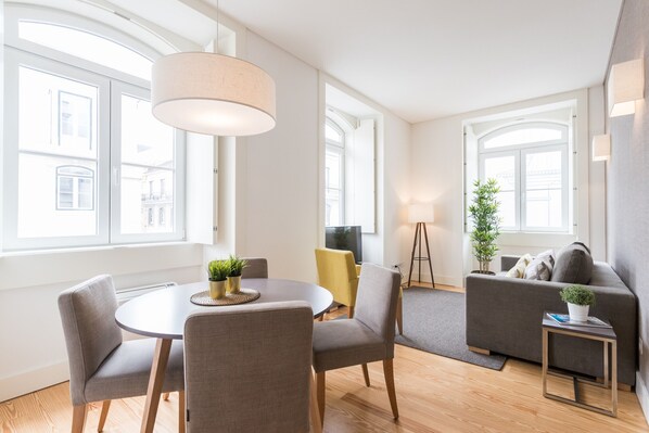 A modern living room with a round dining table, grey sofas, and a small side table.