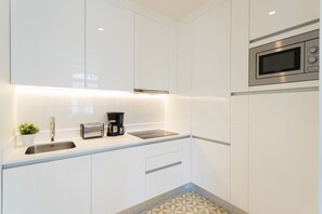 A modern kitchen with white cabinets, a stainless steel sink, a toaster, a coffee maker, and a microwave.