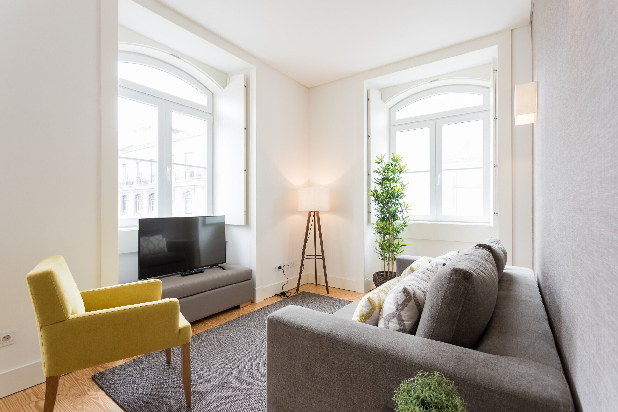 Una sala de estar moderna con un sofá gris, un sillón amarillo, un televisor y una lámpara de pie.