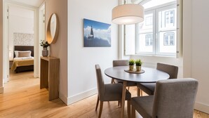 A modern dining area with a round table, chairs, and a pendant light. A painting of a sailboat is on the wall, and there is a bed visible in the background. - FLH Downtown Fantastic Flat (Lisbon)