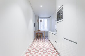 Uma cozinha estreita com piso de padrão geométrico, uma janela e um micro-ondas.