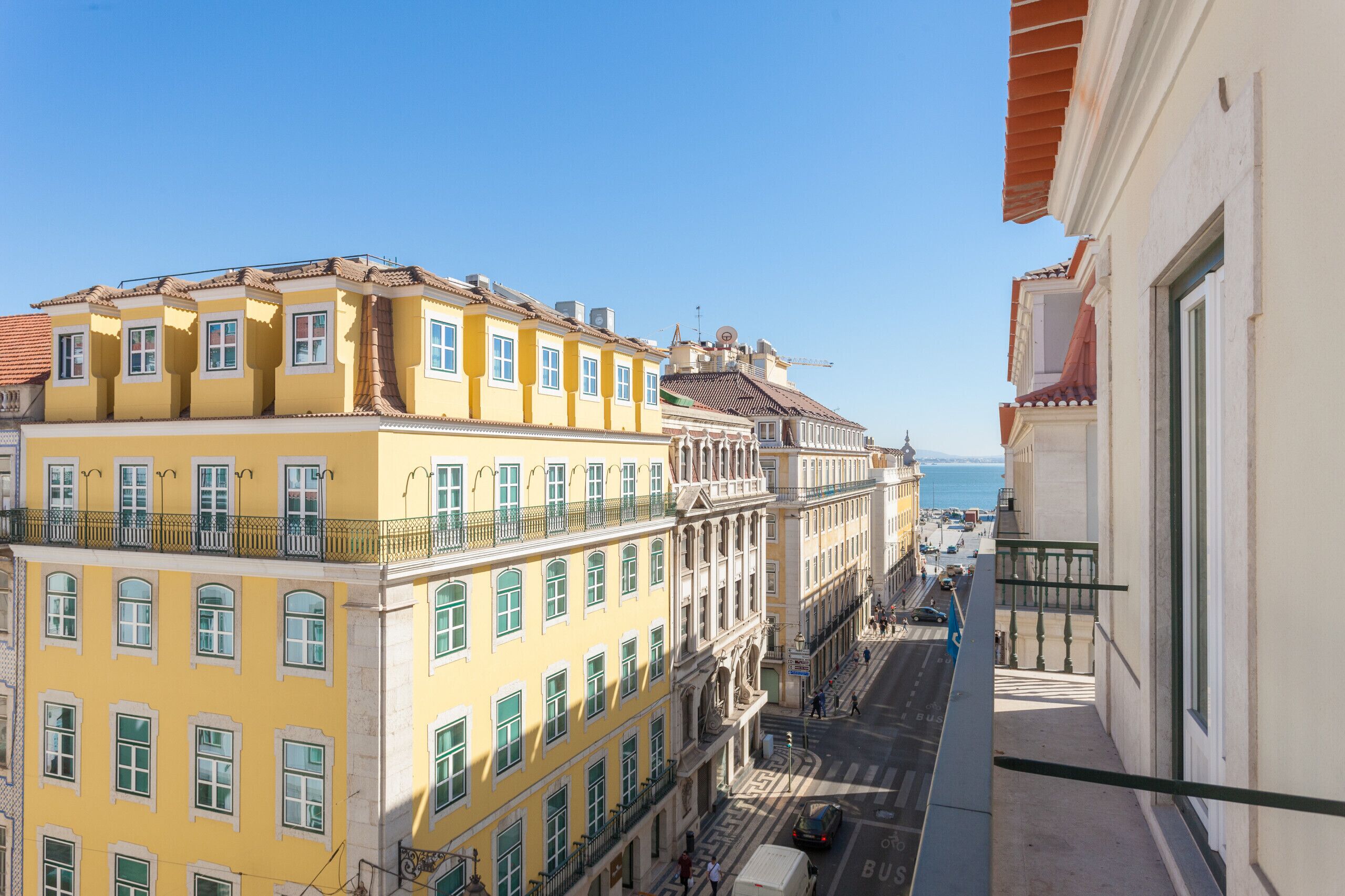 A yellow building with multiple floors, balconies, and a view of the sea.