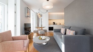 A modern living room with a grey sofa, a pink armchair, a round coffee table, and a dining area with a glass table and chairs.