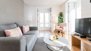 A modern living room with a grey sofa, a coffee table, a TV, and a door leading to a balcony.