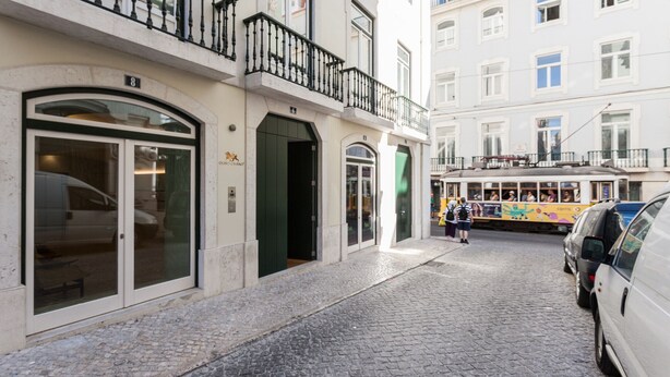 A cobblestone street with a tram, buildings with balconies, and parked cars.