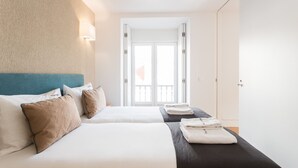 A hotel room with two beds, a view through an open door, and a wall-mounted light fixture.