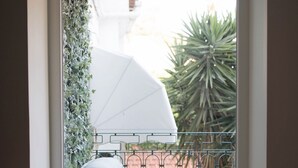 En balkon med en seng, hvid parasol og en potteplante.