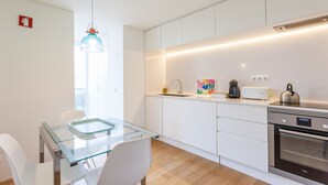 Et moderne køkken med hvide skabe, et glasbord og en indbygget ovn.