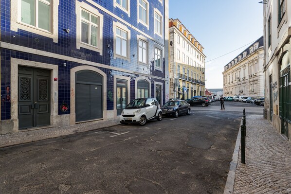 A street with parked cars, buildings with blue and white facades, and a cobblestone sidewalk.