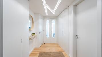 A modern hallway with white walls, wooden flooring, and a central door with a window.