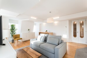 A modern living room with a grey sofa, wooden flooring, a small table, and a TV.