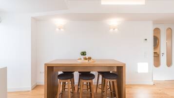 A modern kitchen with a wooden table and three bar stools, a small plant on the table, and recessed lighting.