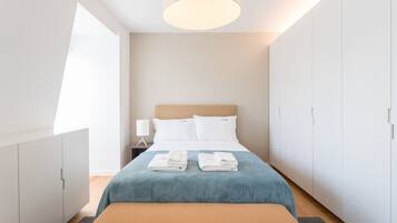 A modern hotel room with a large bed, a bedside table with a lamp, and a wardrobe.
