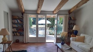 A cozy living room with a white sofa, a coffee table, and a bookshelf. There is a sliding glass door leading to an outdoor patio area.