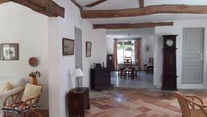 A room with exposed wooden beams, a dining area with a table and chairs, a clock, and a door.