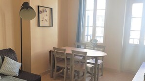 Uma sala de estar aconchegante com sofá, mesa de centro, mesa de jantar com cadeiras, luminária pendente e janela com cortinas.