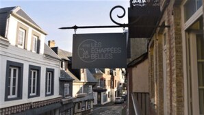 Uma rua estreita com edifícios em ambos os lados, uma placa pendurada em uma varanda e céu claro.