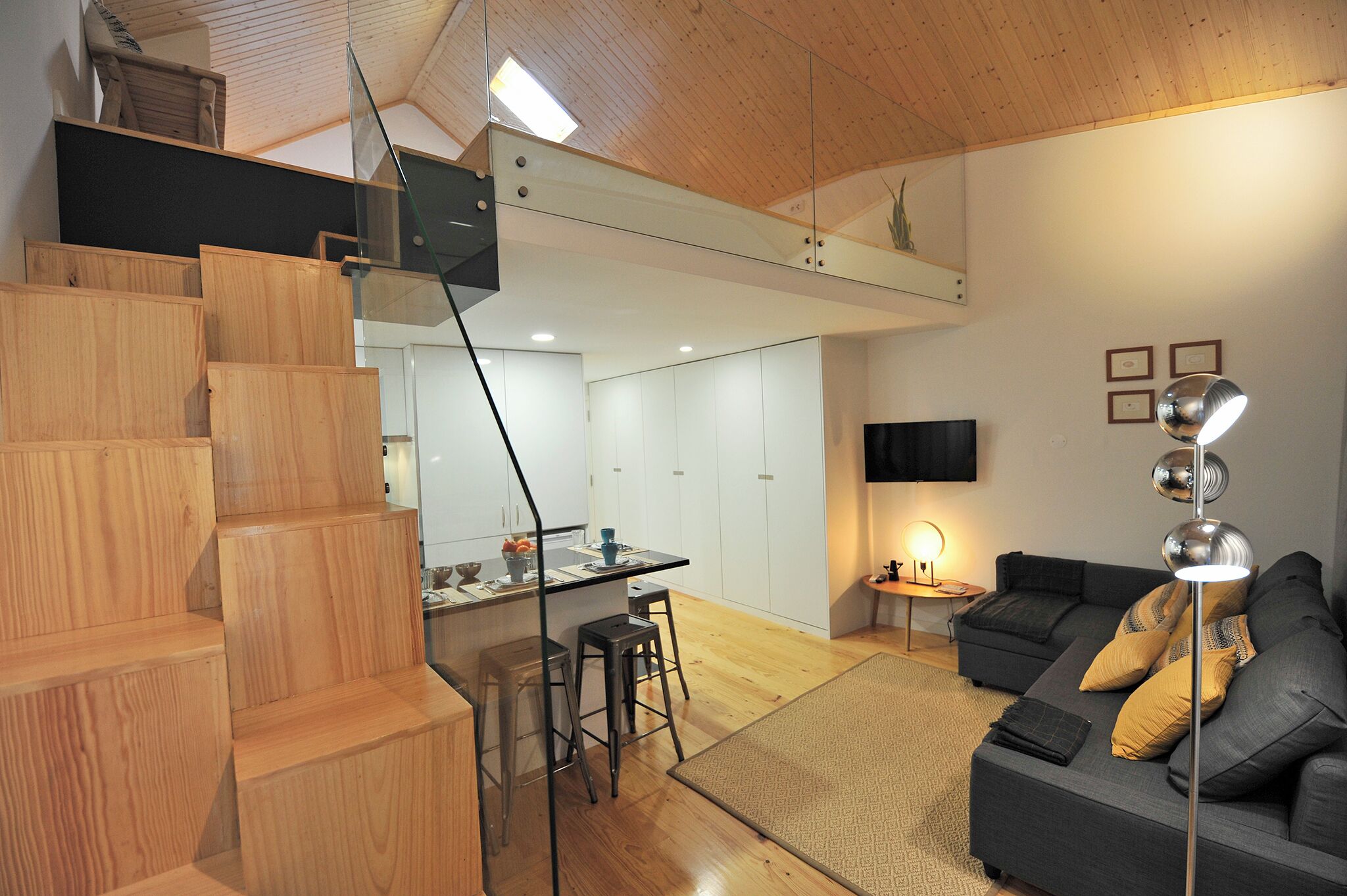 A modern interior with a wooden staircase, a dining area, a sofa, and a flat-screen TV.