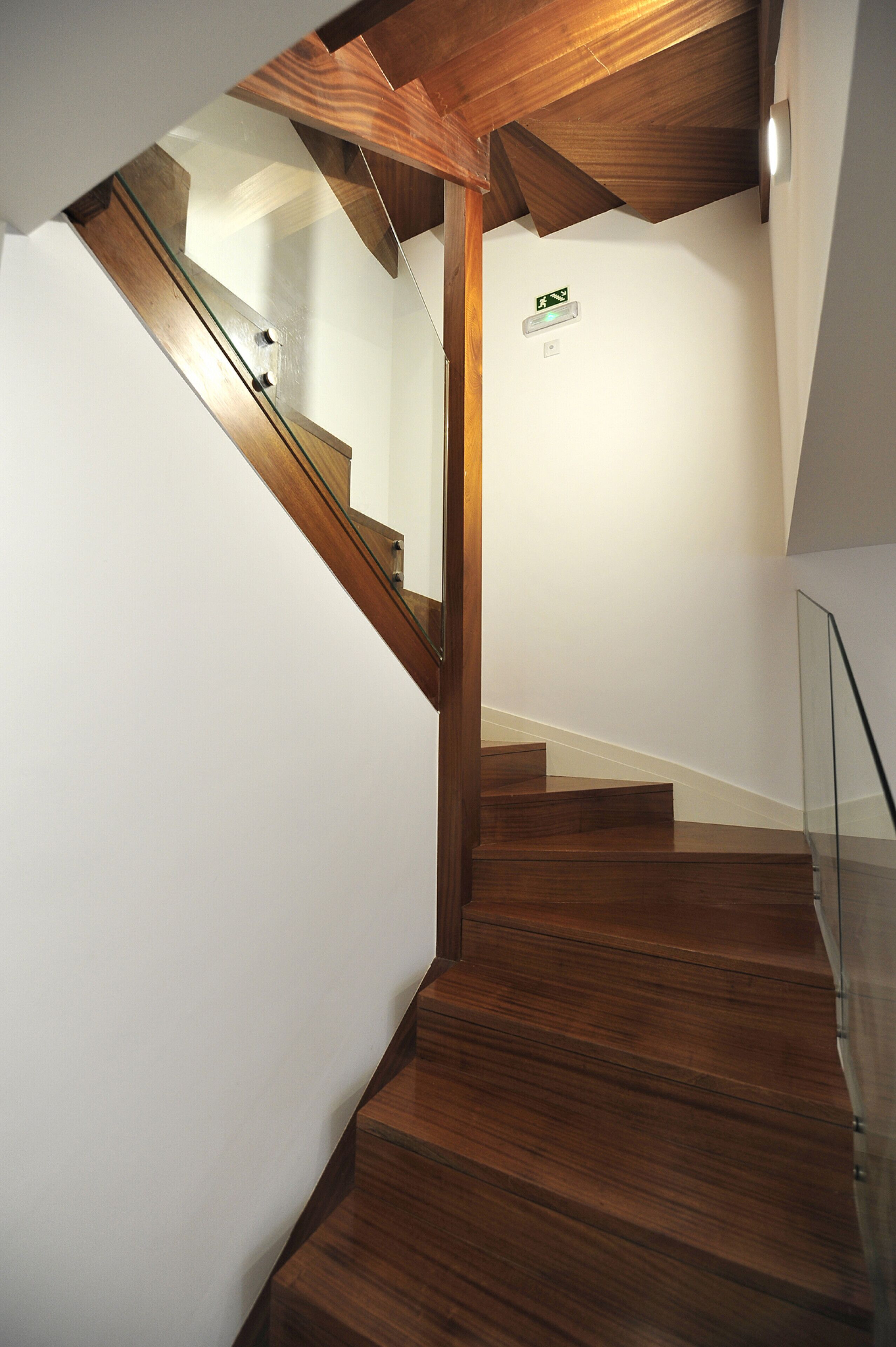 Un escalier en bois avec des rampes en verre, des murs blancs et un plafond avec des poutres en bois.